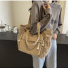 A woman is holding a beige corduroy shoulder bag with a zipper on her shoulder while standing in front of a dark counter.