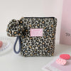 A leopard print makeup bag with a gold zipper and gray strap resting on a white surface.