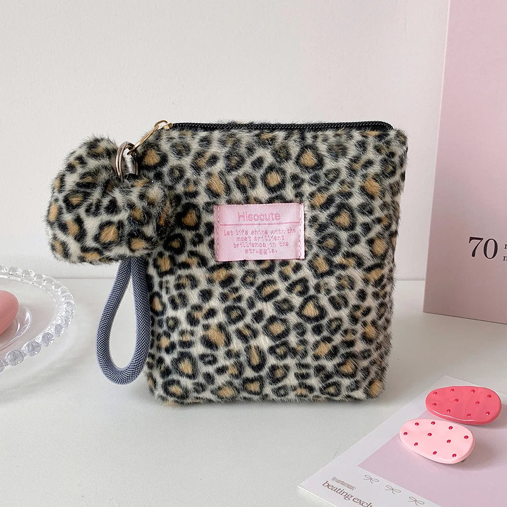 A leopard print makeup bag with a gold zipper and gray strap resting on a white surface.