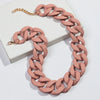 A necklace made of matte pink acrylic links with a gold chain, displayed on a white box.