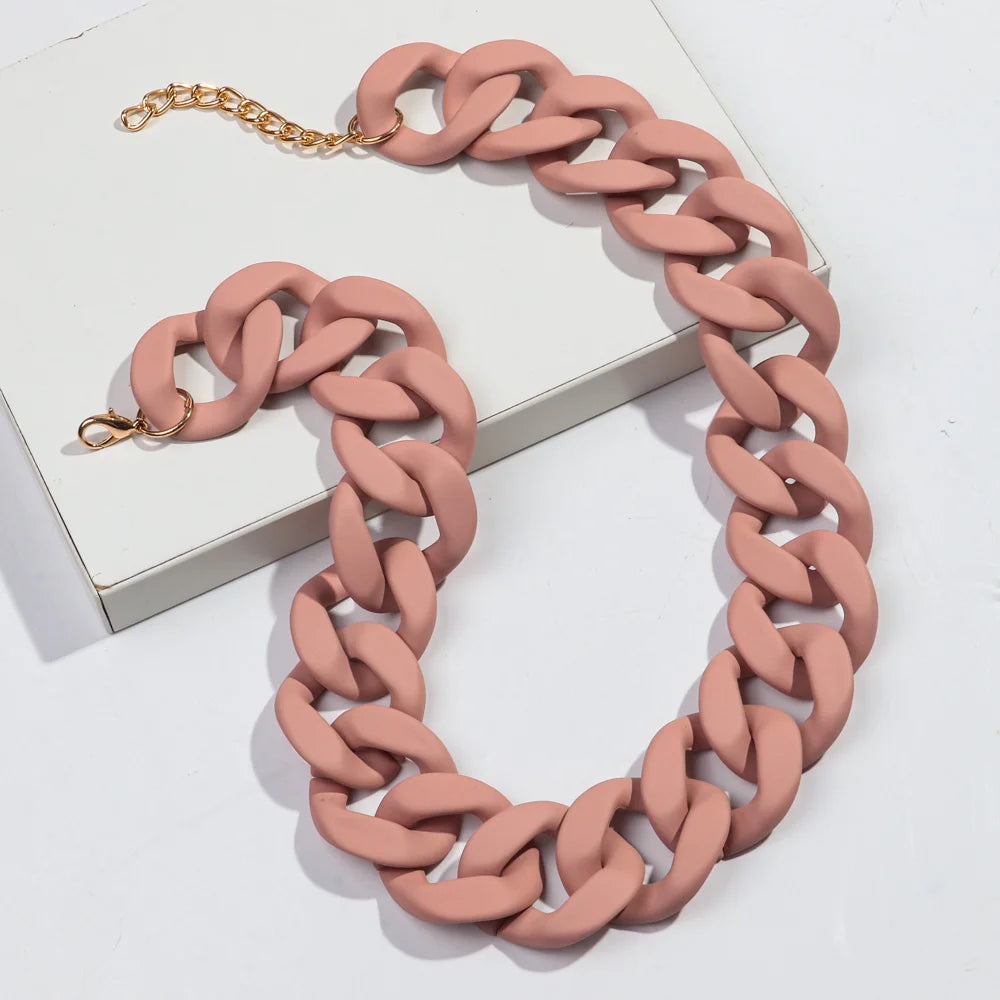 A necklace made of matte pink acrylic links with a gold chain, displayed on a white box.