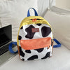 A yellow and black cow print fashion backpack resting on a white surface next to a silver laptop.