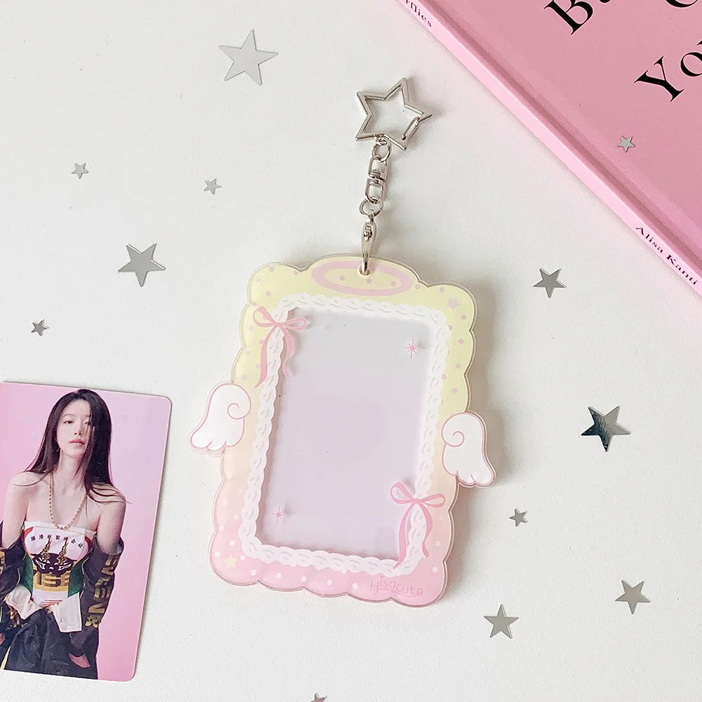 A clear display case framed in pink and yellow, featuring angel wings, suspended by a silver charm.