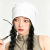 A close-up of a woman wearing a white slouchy knit beanie hat and a olive green top with long black hair.