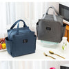 A dark blue insulated canvas tote bag with double pockets resting on a white surface next to a laptop and a glass container.