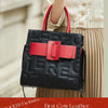 A black leather shoulder bag with a red accent strap and gold hardware being held by a person.