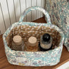 A light blue and cream quilted fabric storage basket with a handle, holding glass jars.