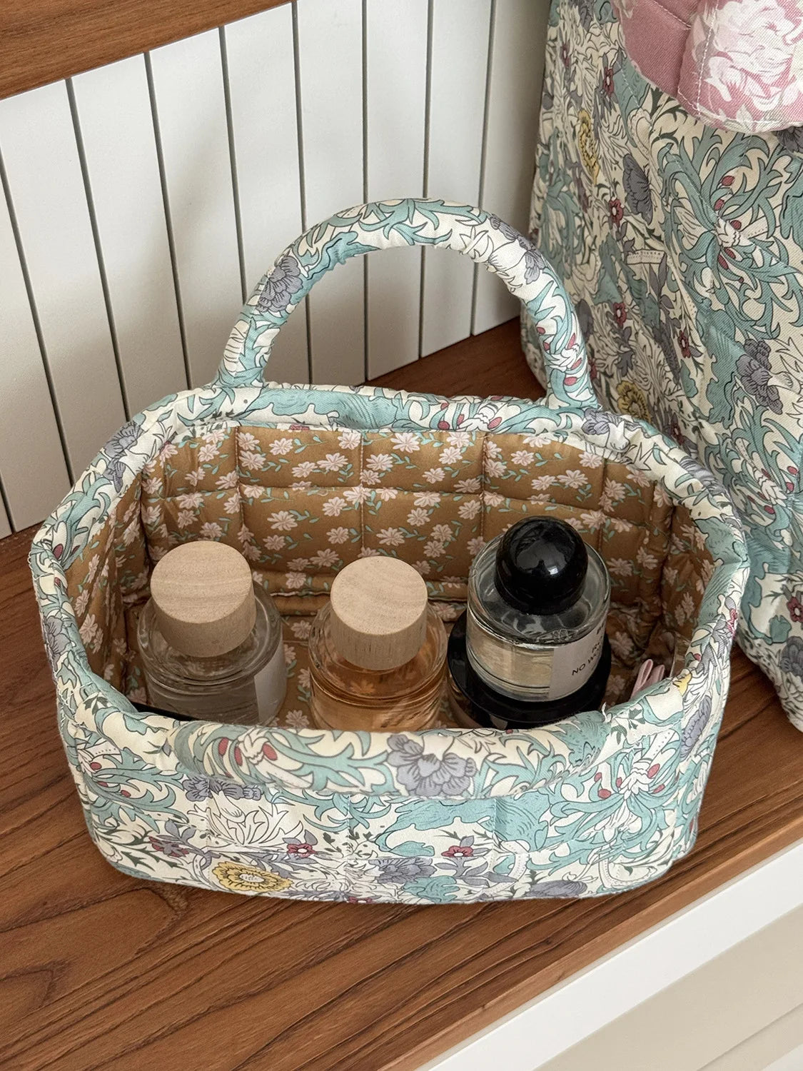 A light blue and cream quilted fabric storage basket with a handle, holding glass jars.