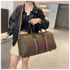 A woman is holding a brown and gold plaid travel duffle bag with black leather straps and a black jacket.