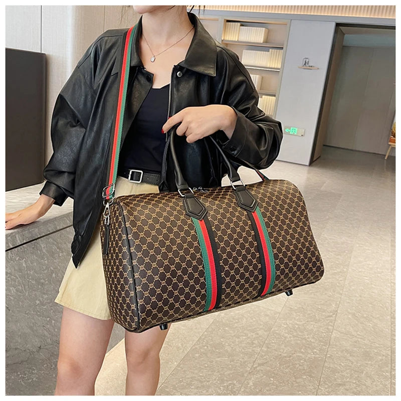 A woman is holding a brown and gold plaid travel duffle bag with black leather straps and a black jacket.