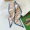 Écharpe de soie couleur crème avec bordure bleue et motif fraise rouge, présentée sur du papier blanc.