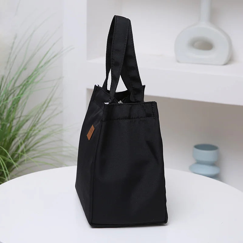 A black durable aluminum foil insulated lunch bag resting on a white shelf.