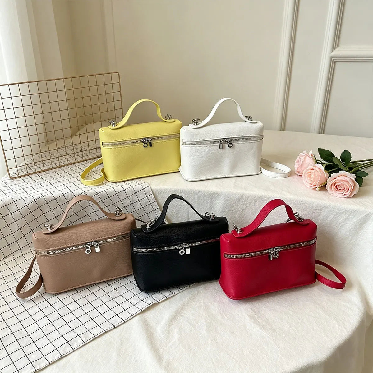 A collection of four minimalist pebbled leather box crossbody bags in yellow, white, black, and red displayed on a white tabl