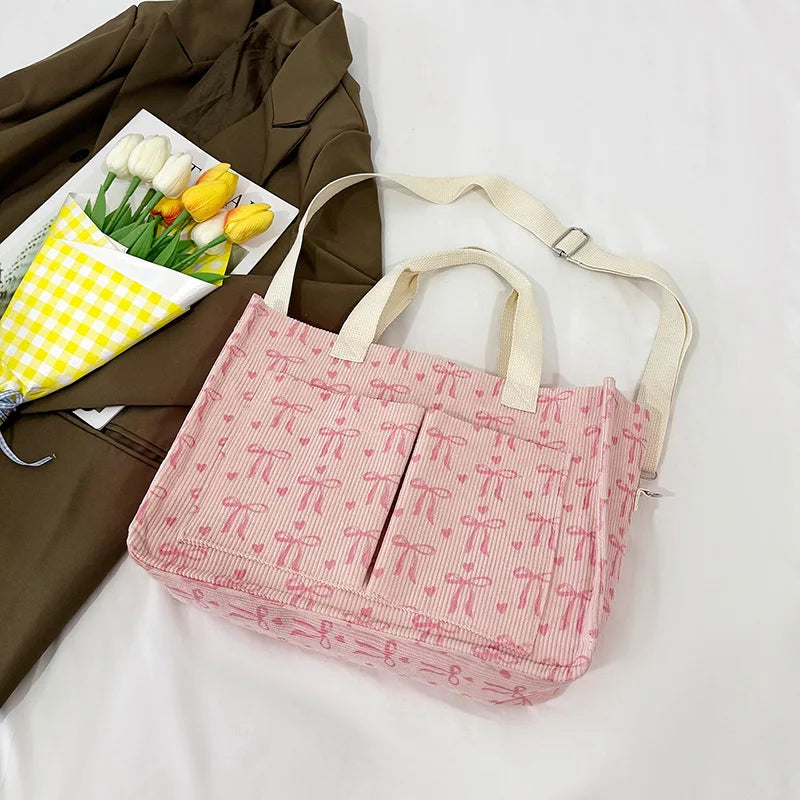 A pink canvas tote bag with a strawberry pattern is shown next to a green jacket and a tray of white tulips.