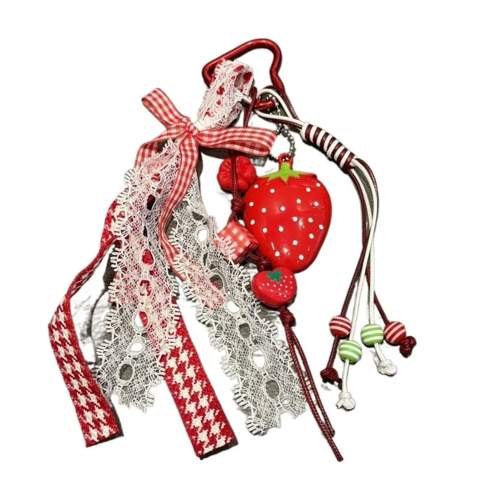 A red strawberry bag charm keychain featuring a decorative ribbon and lace detail.