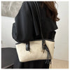 A black coat sleeve shows a cream leather tote bag with black strap and gold hardware.