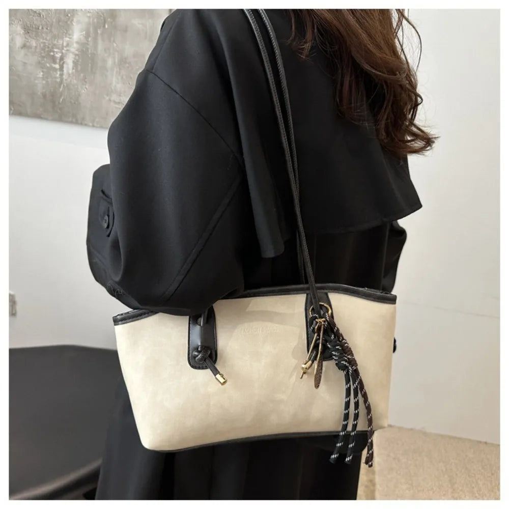 A black coat sleeve shows a cream leather tote bag with black strap and gold hardware.