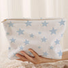 A white corduroy cosmetic bag with a light blue starfish pattern being held by a hand.
