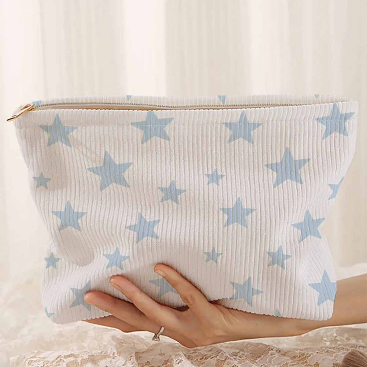 A white corduroy cosmetic bag with a light blue starfish pattern being held by a hand.