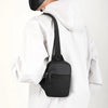 A black canvas crossbody sling bag is shown attached to a white hoodie.