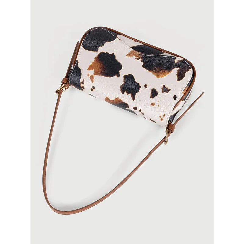 A single shoulder bag featuring a cow print pattern in beige and brown on a tan background.
