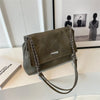 Bolso de cuero retro verde oliva oscuro con cadena colgado sobre una superficie blanca junto a una foto enmarcada.