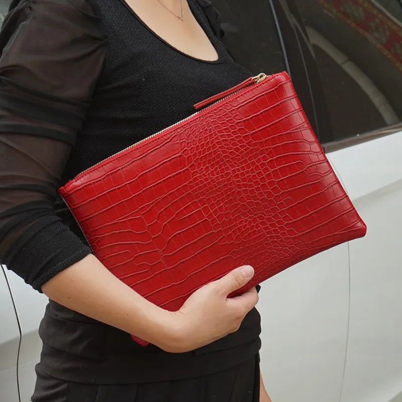 A woman holds a red alligator print clutch bag against a black top.