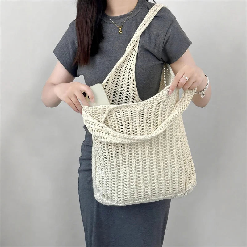 A woman holds a cream-colored bohemian knit shoulder bag made of crocheted yarn against a gray background.