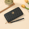 A black patterned zipper wallet with gold accents resting on a light background next to a vintage watch.