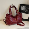 A deep burgundy leather shoulder bag with a strap is displayed on a white surface next to a framed sign.