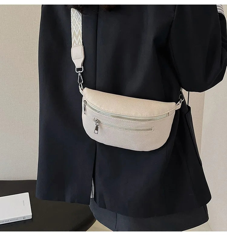 A black blazer features a cream leather multi-pocket crossbody bag with a white patterned strap.