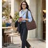 A woman wearing a blue shirt and dark pants carries a brown quilted nylon shoulder bag while walking outdoors.
