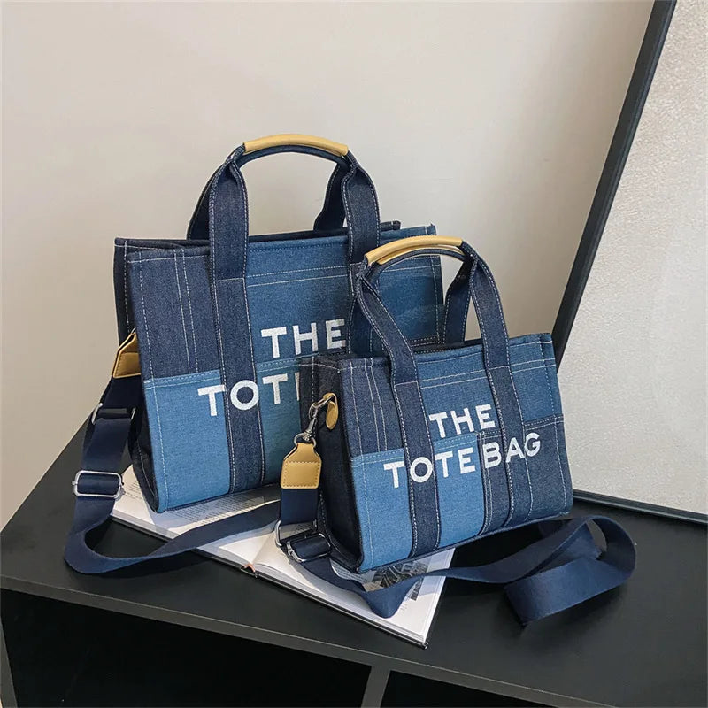 A navy blue canvas tote bag with light blue accents and tan leather handles resting on a white surface.