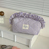 A lavender checkered makeup pouch with a ruffled lace trim resting on a white shelf.