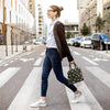 Une femme en blazer foncé et jeans marche sur un passage piéton tenant un sac à lunch en tissu noir.