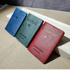 Three genuine leather passport holders in blue, green, and red resting on a light wooden surface.
