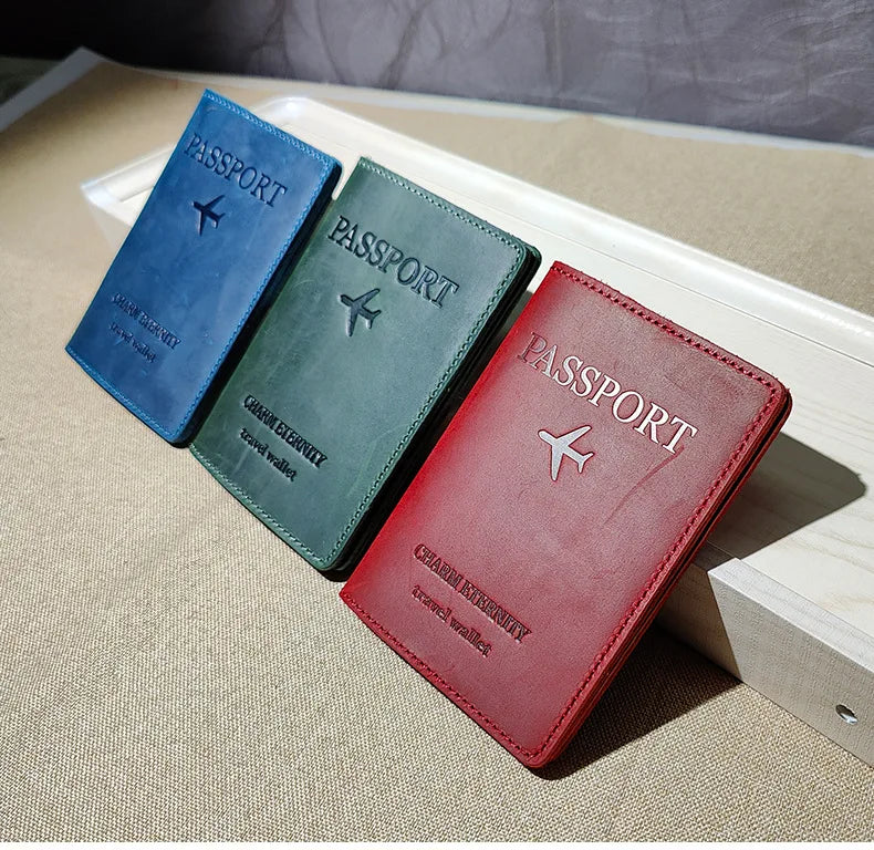 Three genuine leather passport holders in blue, green, and red resting on a light wooden surface.