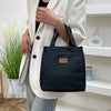 A woman holds a black insulated lunch bag in front of a white blazer and light blue jeans.