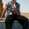 A man wearing a denim shirt and black pants is posing with a brown leather sling backpack.