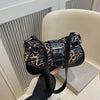 Un sac à main en similicuir à imprimé léopard noir tenu par une main sur un fond clair.