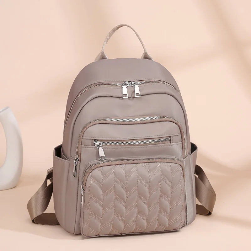 A light beige waterproof women's travel backpack with a quilted design and silver zippers.