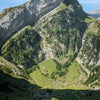 Landschaft mit steilen grünen Hängen und Wasser unter blauem Himmel