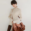 Eine Frau präsentiert einen braunen Vintage-Soft-PU-Leder-Schultertasche und einen braunen Rollkragenpullover.