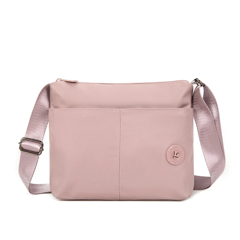 A light pink waterproof nylon crossbody bag with a flap closure and adjustable strap.