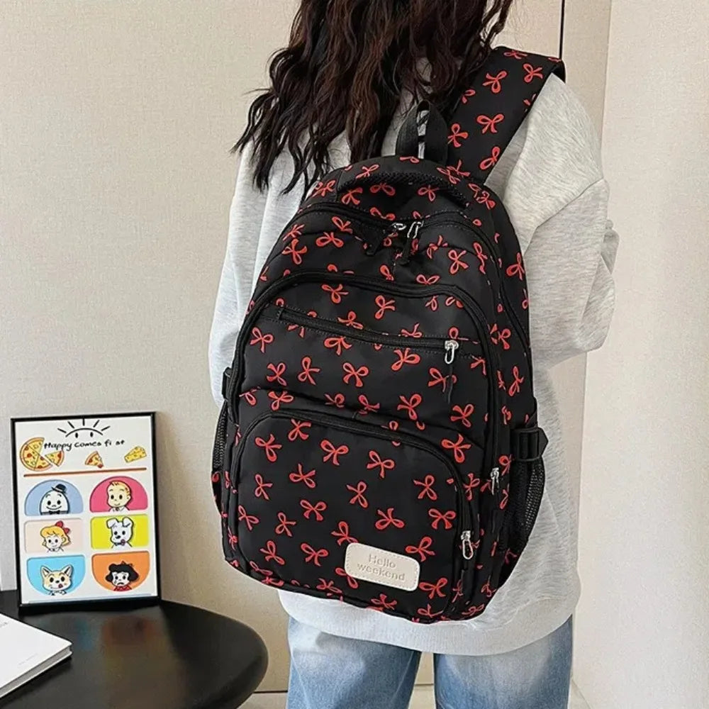 A black nylon travel backpack with a red bow print is worn by a person.