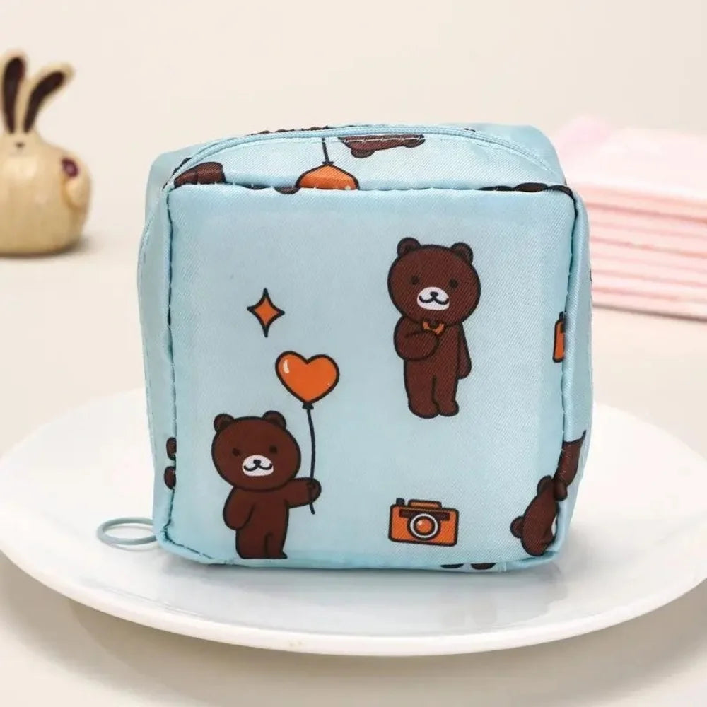 Light blue fabric pouch with brown bear and orange heart embroidery for sanitary napkin storage.