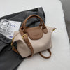 A beige vintage PU leather crossbody handbag with tan leather trim resting on a gray fabric.