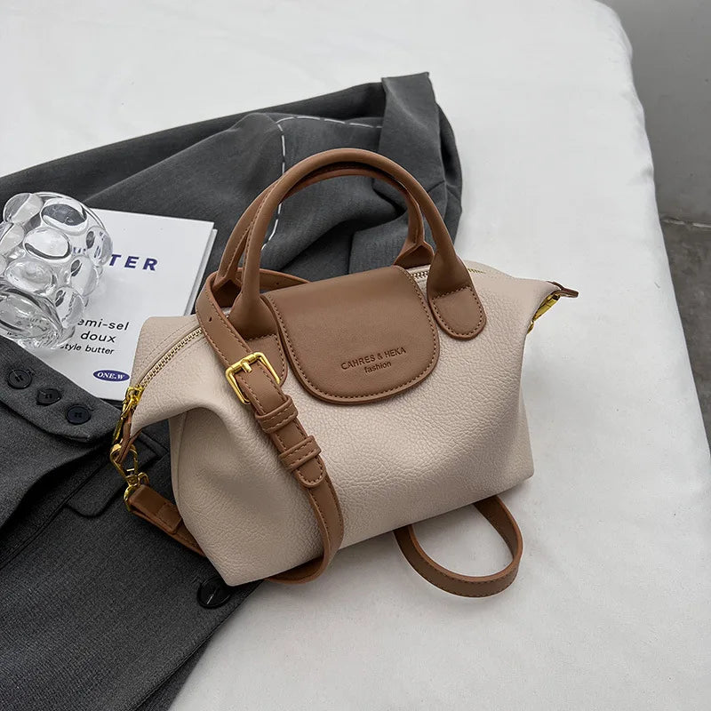 A beige vintage PU leather crossbody handbag with tan leather trim resting on a gray fabric.