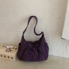 A purple plaid nylon drawstring tote bag is displayed on a light surface against a white wall.