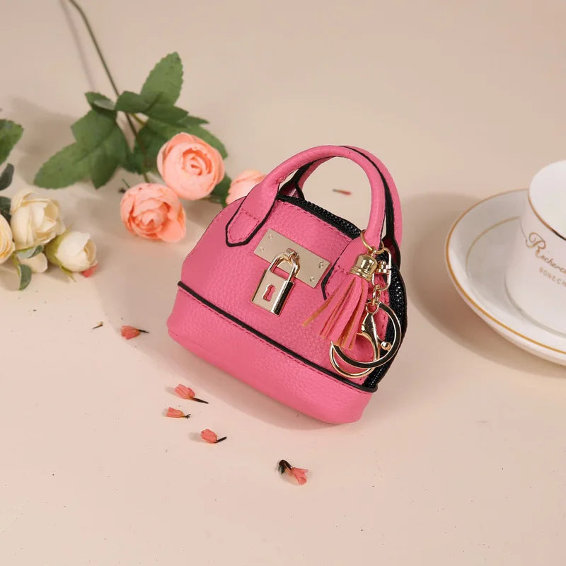 A pink portable earbud case with a black strap and gold keychain charm rests on a light background.